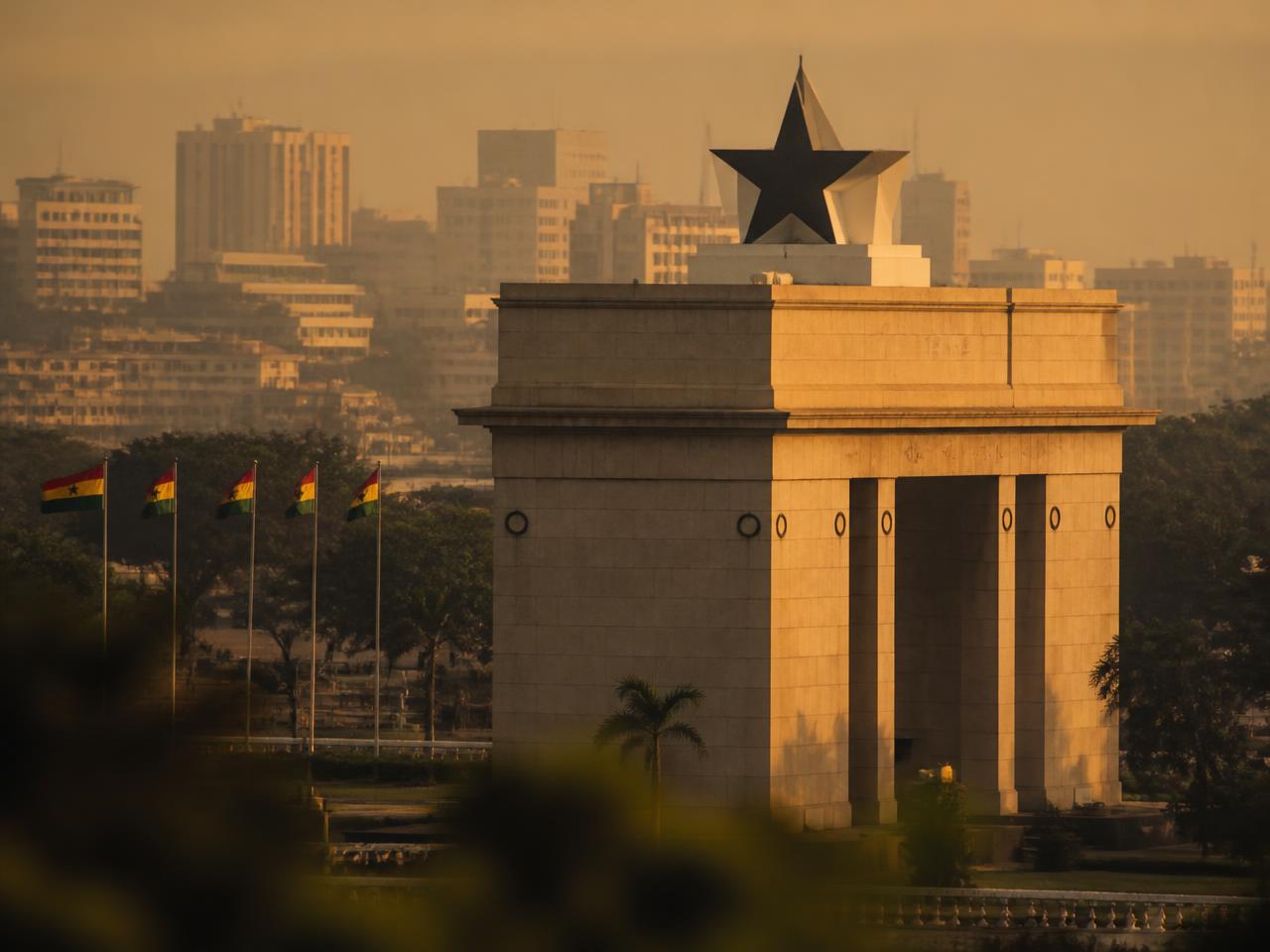 Black Star Independence Arch in Accra, Ghana, at golden hour with Ghanaian flags flying nearby